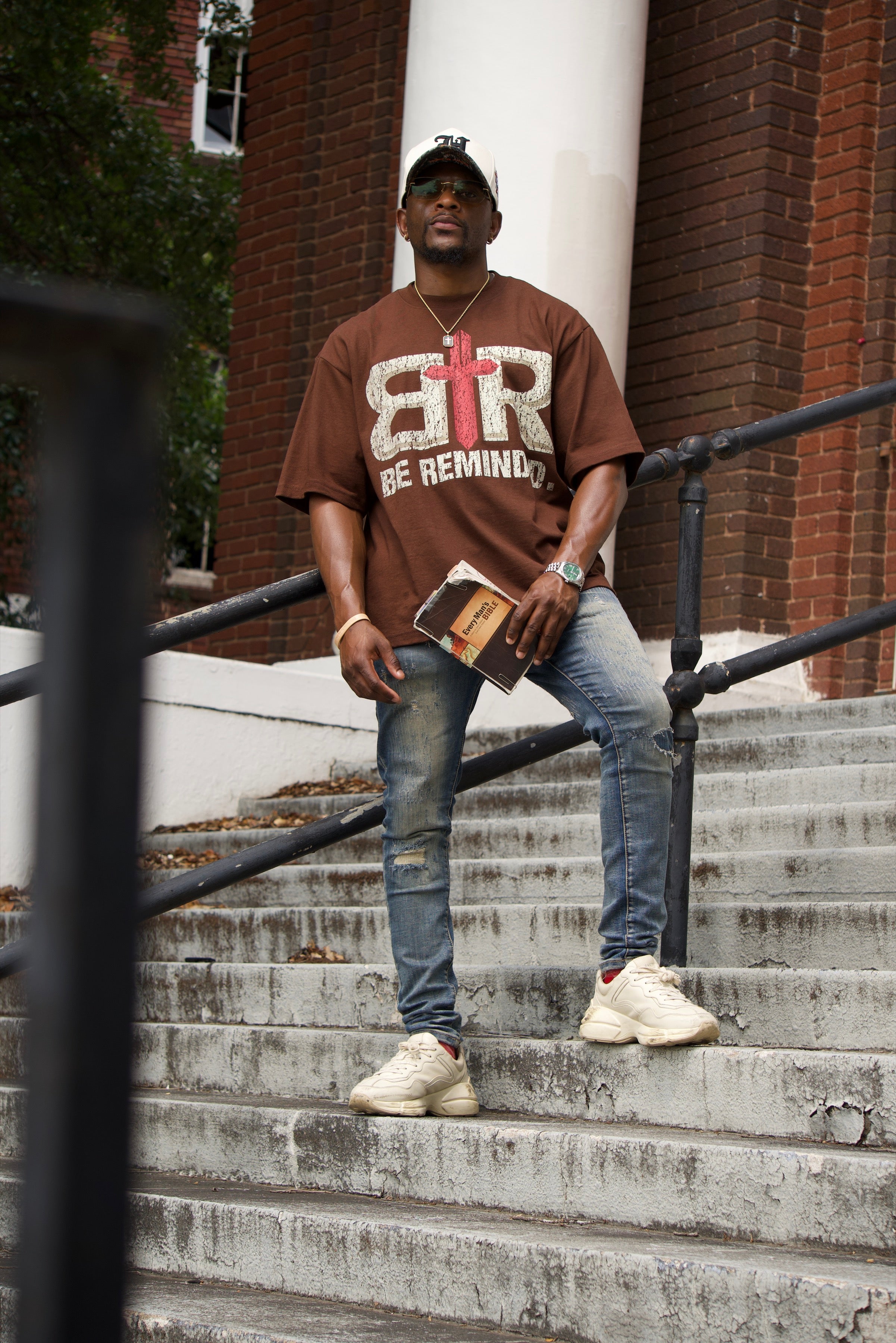 Model wearing the Be Reminded B R cross logo shirt on church steps in Dallas